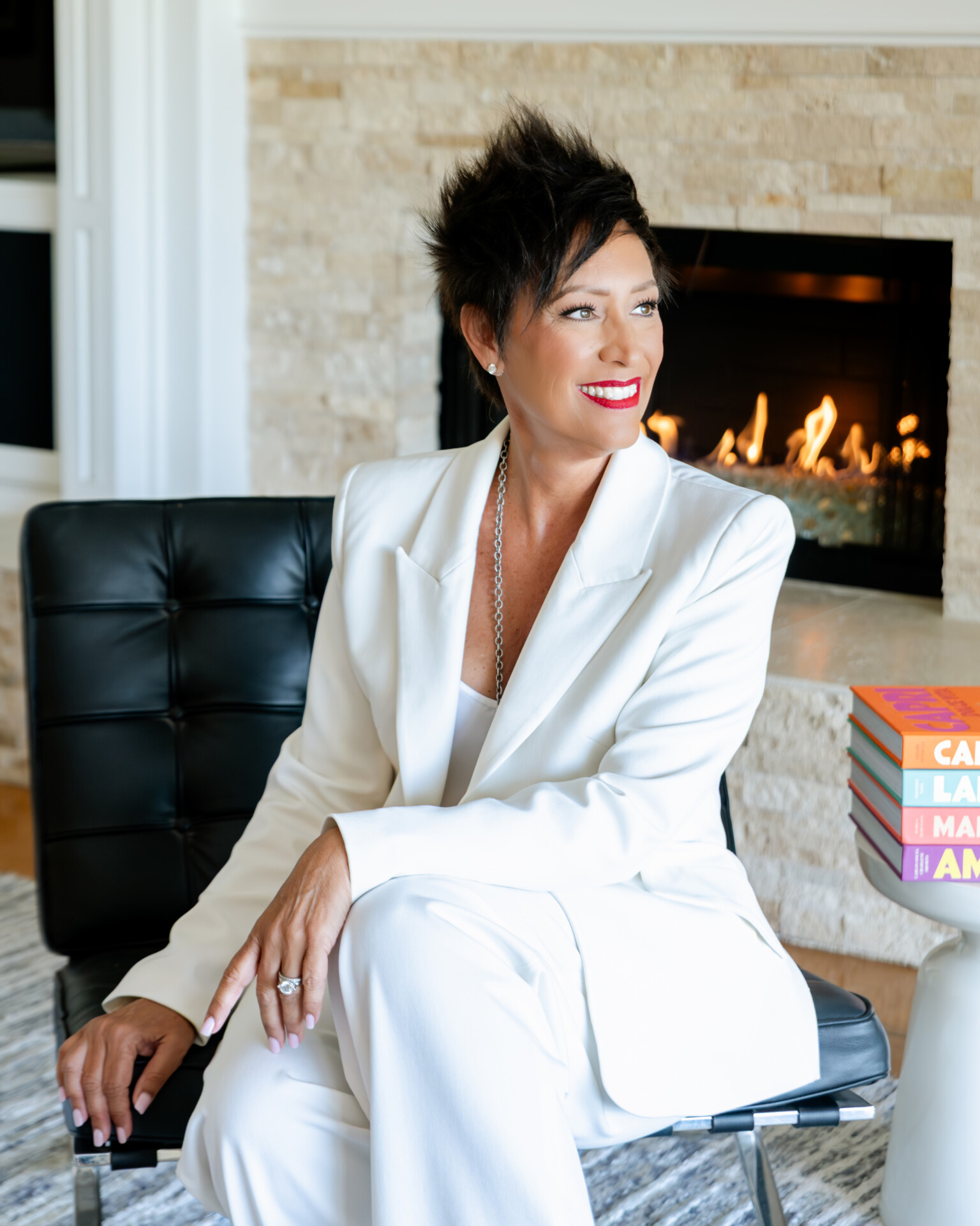 Gina Maier Vincent seated in a white suit beside a fireplace